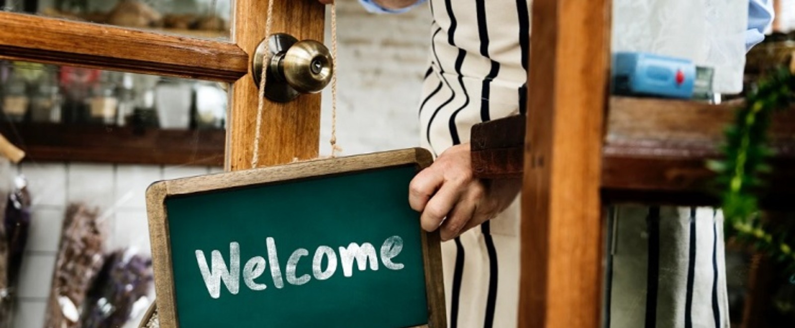 a small business person placing a welcome sign on a doorknob

